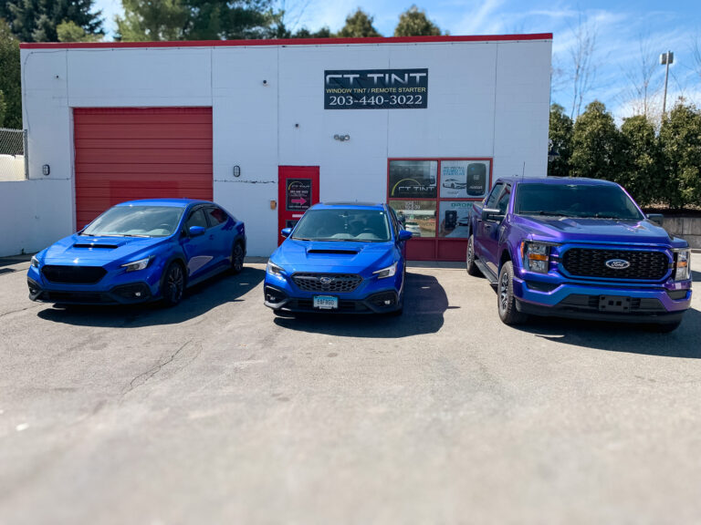 Three vehicles with dark tinted windows parked outside an auto window tint shop