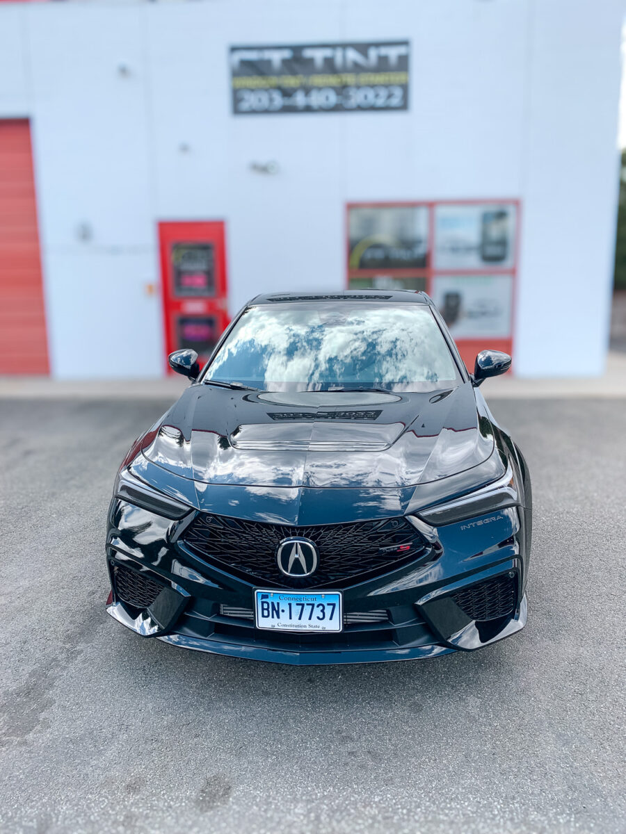 Front view of a black sedan parked outside a window tint shop, showcasing tinted side windows for added privacy and UV protection.