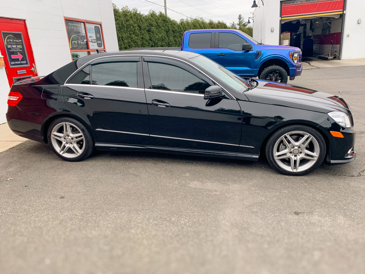 Black sedan with dark window tint parked outside an auto tint shop, showing tinted side windows for privacy and UV protection.