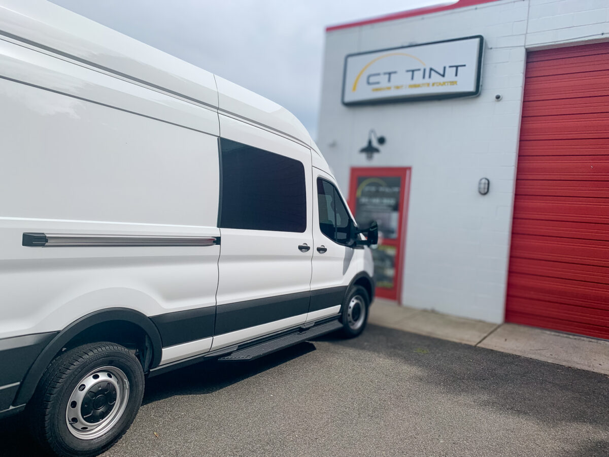 White cargo van with dark tinted side windows parked outside an auto window tint shop for added privacy and UV protection