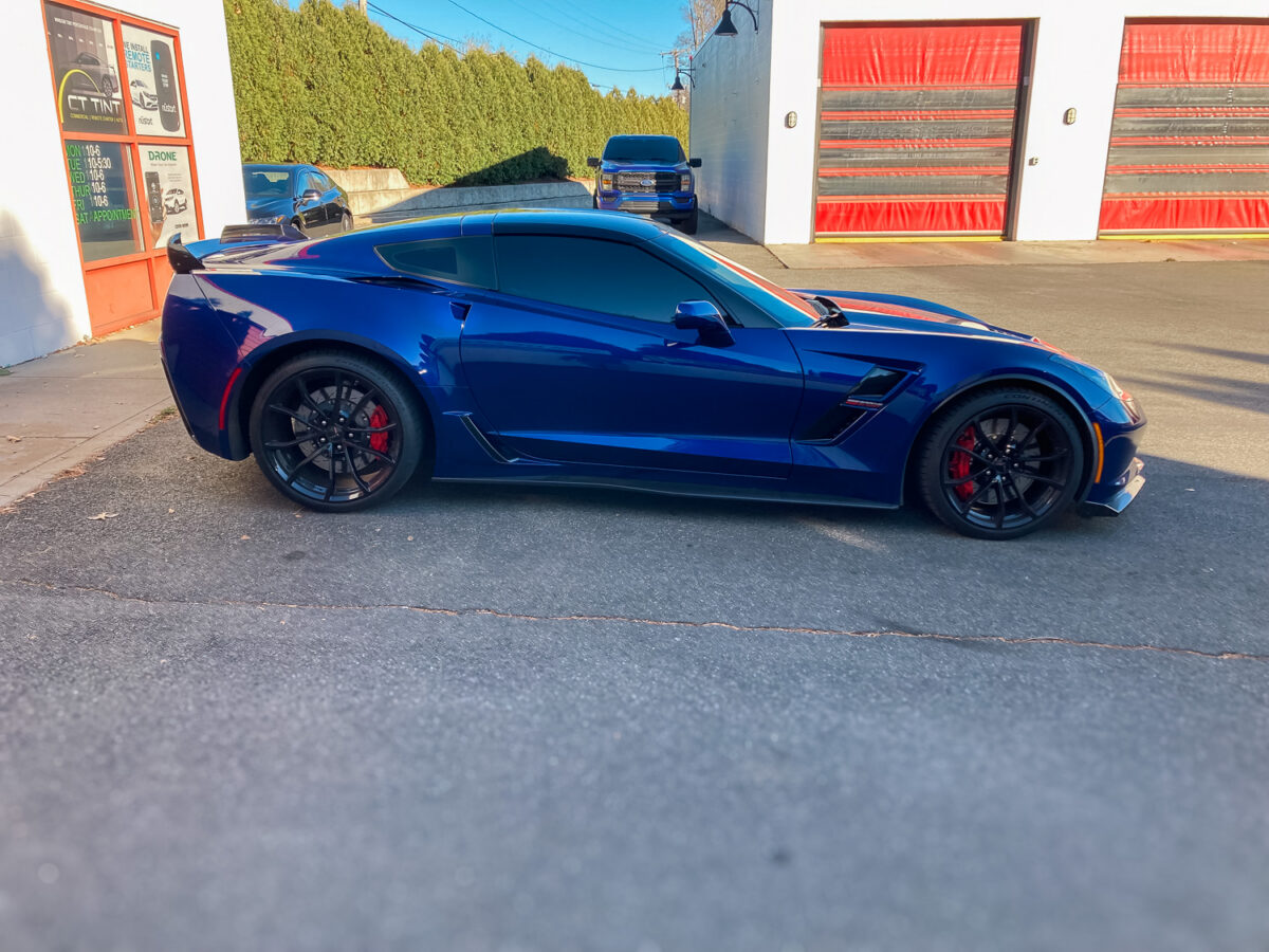 Blue sports car with dark window tint parked outside an auto tint shop, highlighting privacy and UV protection for side windows.