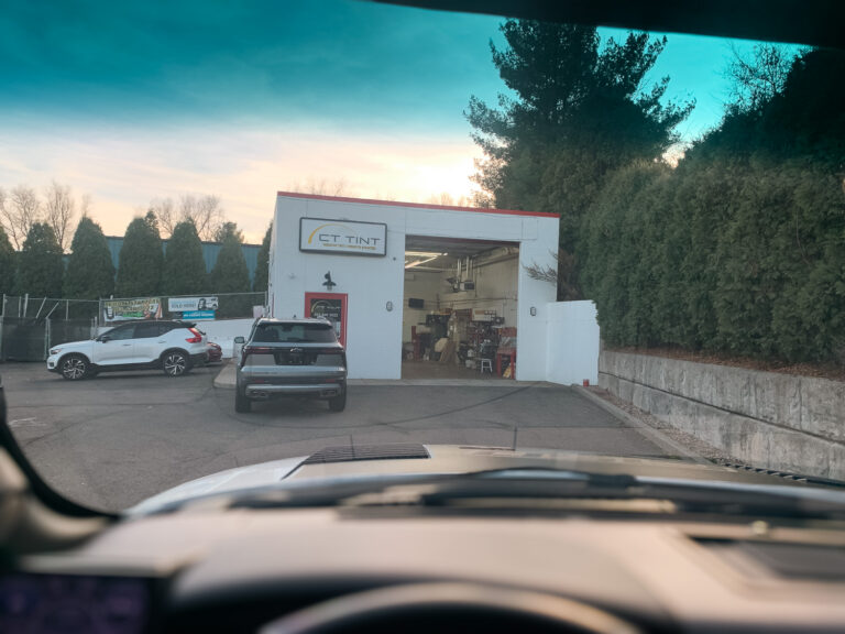 View from inside a vehicle approaching an auto window tint shop, showing tinted glass and a service bay for privacy, heat rejection, and UV protection.