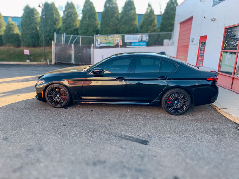 Black sedan with dark tinted side windows parked outside an auto window tint shop for added privacy and UV protection