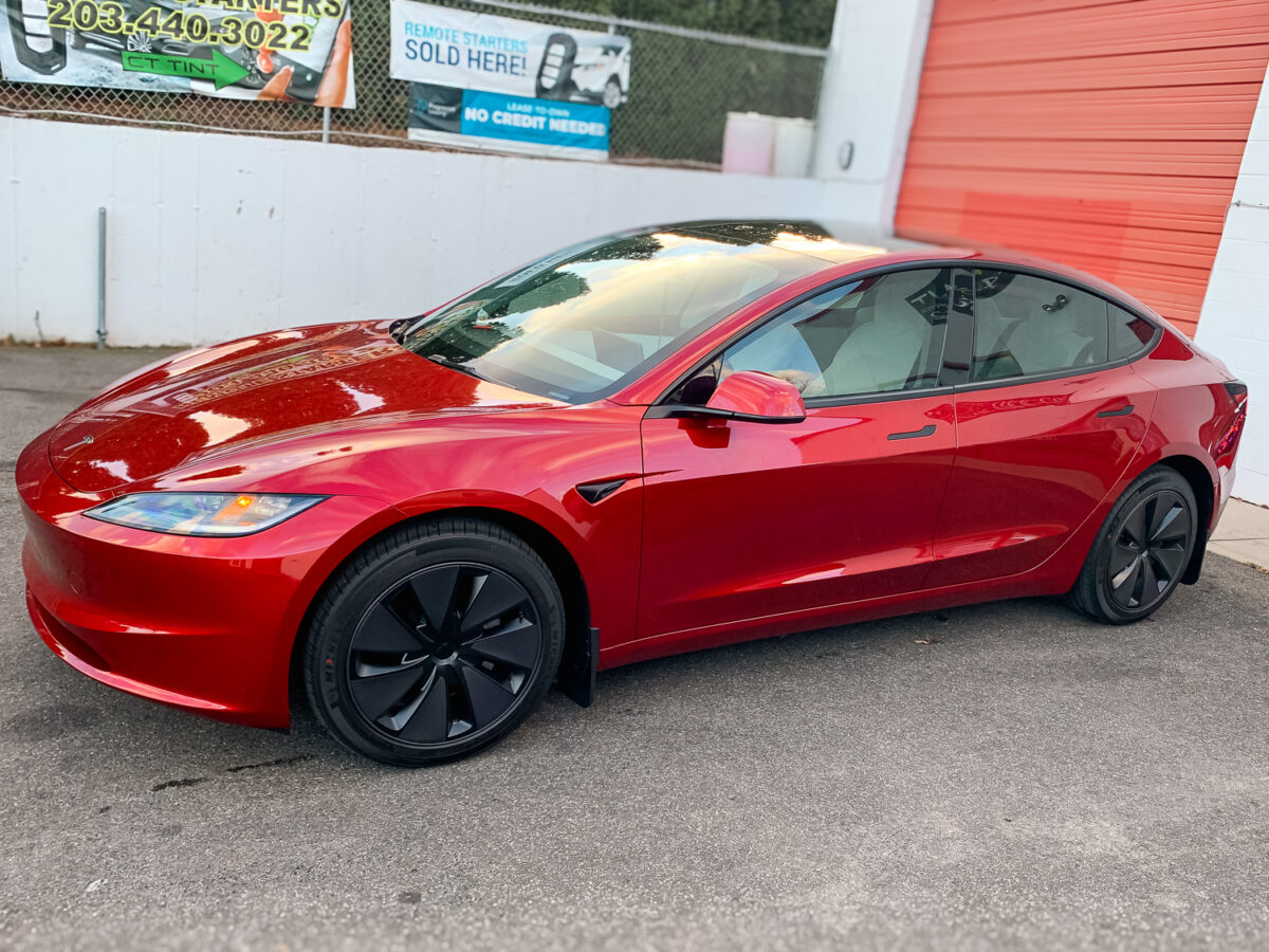 Red sedan parked outside a tint shop with dark tinted side and rear windows for added privacy and UV protection
