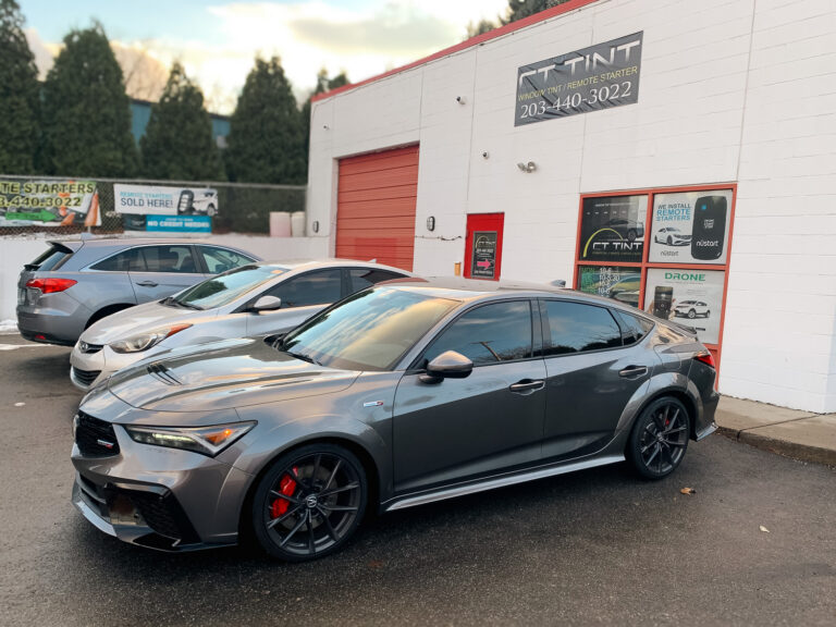 Gray sedan with dark tinted side windows parked outside an auto window tint shop, highlighting privacy and UV protection.