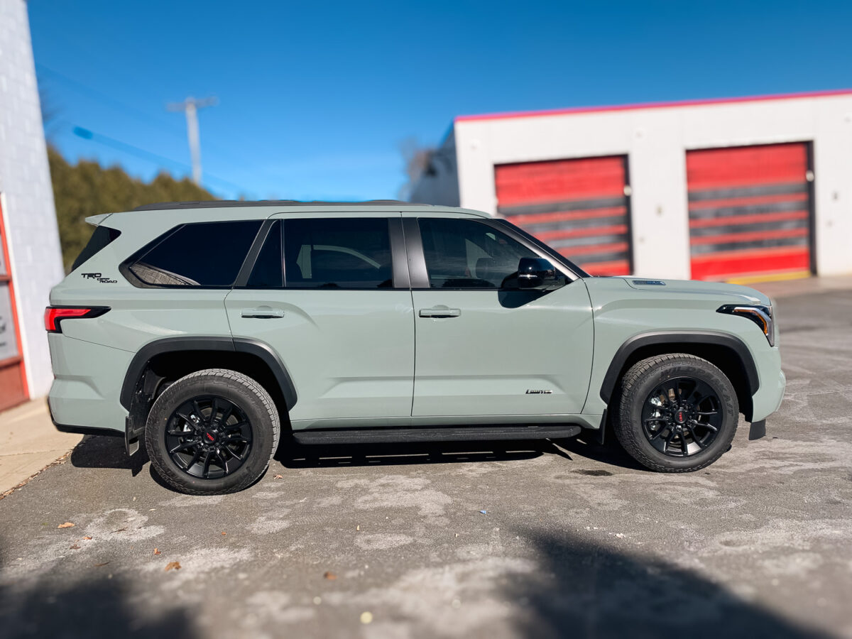 Side view of a light-colored SUV with dark tinted side and rear windows outside an auto shop