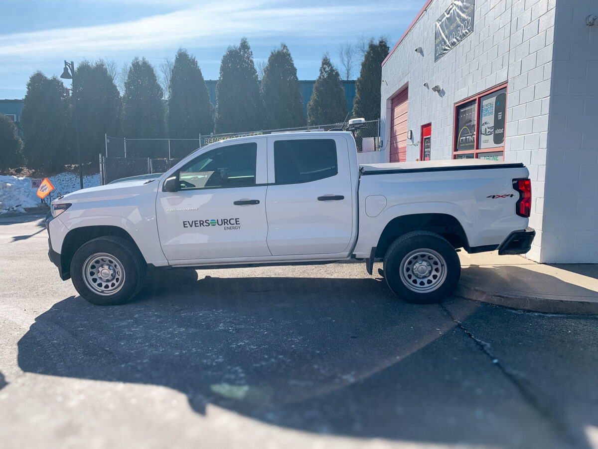 White crew cab pickup truck with dark tinted side windows parked outside an auto window tint shop for added privacy and UV protection.
