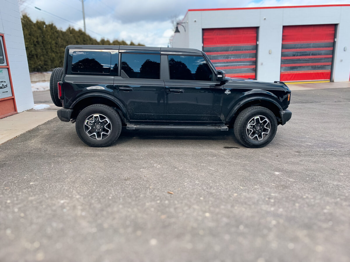 Black SUV with dark tinted side windows parked outside an auto shop, showing privacy window tint.